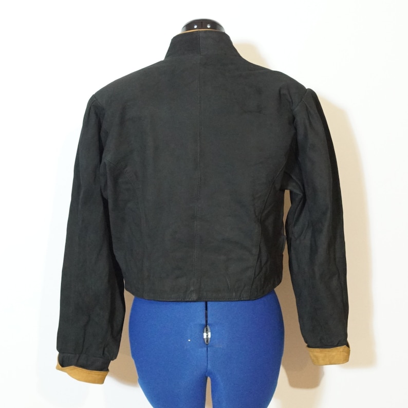 May include: A black cropped jacket with long sleeves and brown suede trim on the cuffs and collar.