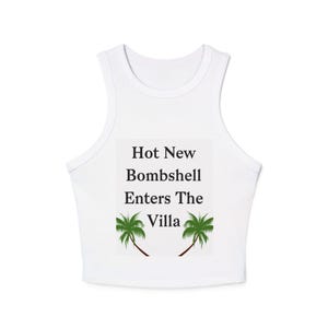 May include: White crop top with a scoop neck and a rectangular graphic. The graphic reads "Hot New Bombshell Enters The Villa" with two green palm trees. A casual, sleeveless top.