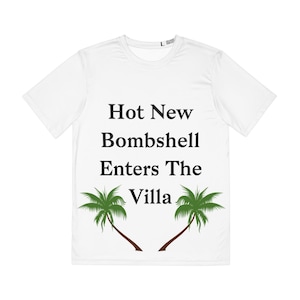 May include: White t-shirt with the text "Hot New Bombshell Enters The Villa" in black. Two green palm trees with brown trunks are below the text. The shirt has short sleeves and a crew neck.