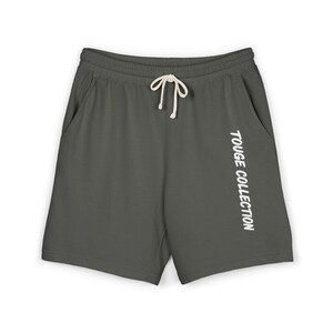 Può includere: Pantaloncini grigio scuro con vita con coulisse e tasche. Il testo "TOUGE COLLECTION" è stampato verticalmente in bianco sulla gamba destra. Questi pantaloncini sono un capo d'abbigliamento casual.