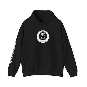 May include: Black hoodie with a white circular graphic on the front, featuring Japanese characters and the text "YONAKA SUPPLY." The left sleeve displays "TOUGE COLLECTION" in white. The hoodie has a drawstring hood and a front pocket.