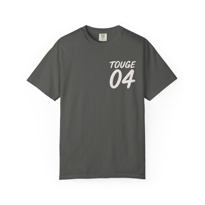 Könnte beinhalten: Dunkelgraues T-Shirt mit dem weißen Aufdruck "TOUGE" und der Nummer "04" auf der Vorderseite. Das Shirt hat kurze Ärmel und einen Rundhalsausschnitt. Der Stoff scheint eine weiche Baumwollmischung zu sein.