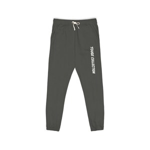 May include: Dark grey sweatpants with a drawstring waist and pockets. The text "TOUGE COLLECTION" is printed vertically down the right leg in white. The pants are made of a soft material.