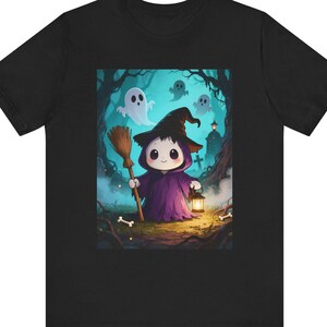 May include: A black t-shirt featuring a graphic print of a small, cute character dressed in a purple robe and a black witch hat. The character holds a broom and a glowing lantern in a dark, misty forest setting with white ghosts and scattered bones.