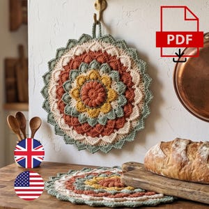 May include: A round, crocheted potholder featuring concentric layers of petals in shades of sage green, terracotta, mustard yellow, and cream. The design includes a central puff stitch flower and a scalloped edge, with a loop for hanging on a wall hook.
