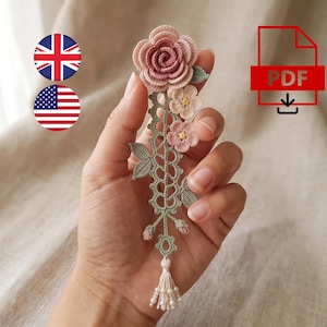 May include: A crochet bookmark featuring a large dusty rose flower at the top, followed by a vertical sage green lace stem with two smaller pale pink flowers, green leaves, and a bottom tassel with small white beads. The design includes a PDF icon.