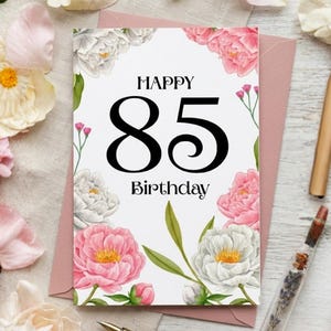 Peut inclure: Une carte de vœux rectangulaire à fond blanc avec le texte noir "HAPPY 85 Birthday" au centre. La carte est ornée d'une bordure florale composée de pivoines roses et blanches, de feuilles vertes et de petits boutons floraux roses.