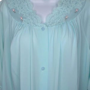 May include: A light blue robe featuring a scalloped lace yoke with delicate pink floral embroidery. The garment has a button-down front closure with matching light blue buttons and a gathered bodice design, providing a soft and flowing silhouette.