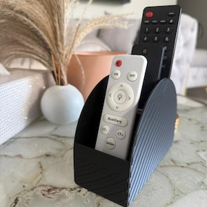 May include: A black, ridged remote control holder containing three remotes. One white remote has buttons labelled "ON", "OFF", "Auxiliary", "CT-", "CT+", and "Section". The other two remotes are black.