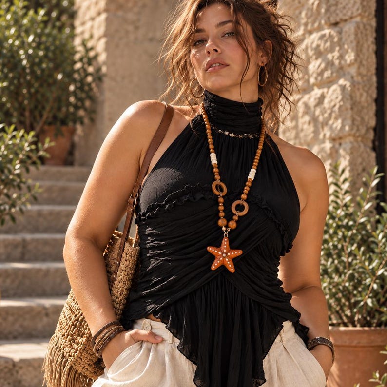 May include: A black sleeveless halter top with a high neck, gathered fabric, and a ruffled hem. The top is accessorized with a long beaded necklace featuring brown wooden beads, white accents, and a large orange starfish pendant with white dots.