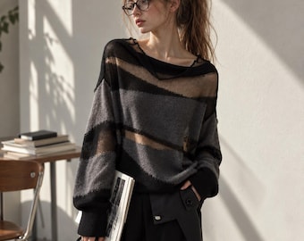 May include: A long-sleeved sweater featuring horizontal stripes in black and charcoal gray, designed with a wide neckline and alternating sheer and opaque knit panels. The garment has ribbed cuffs and a relaxed fit, showcasing a textured knit pattern.