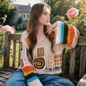May include: A long-sleeved crochet sweater featuring a cream-colored base with a variety of colorful granny square motifs and horizontal stripes in shades of orange, yellow, green, and blue, finished with a V-neckline and a loose, relaxed fit.