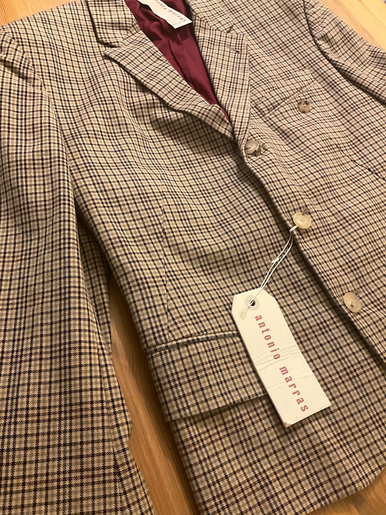 Puede incluir: Una blazer a cuadros beige y negro con forro burdeos. La blazer presenta un dise&ntilde;o cl&aacute;sico con botones y una etiqueta que dice "antonio marras". La chaqueta es de corte entallado.