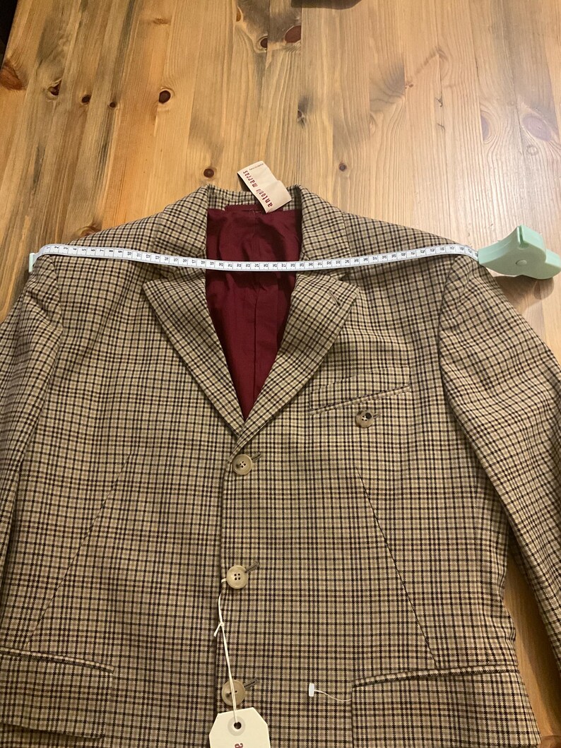 Puede incluir: Una blazer a cuadros marr&oacute;n y beige con forro burdeos. La blazer tiene un cierre cl&aacute;sico de dos botones y solapas con muescas. Una cinta m&eacute;trica est&aacute; colocada sobre los hombros. La etiqueta dice "antiquit&eacute;s".