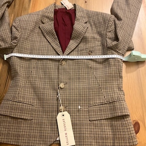 Puede incluir: Una blazer a cuadros marr&oacute;n y beige con forro burdeos. La blazer tiene dos bolsillos delanteros, tres botones y una etiqueta "antonio marras". Una cinta m&eacute;trica est&aacute; colocada sobre la blazer.