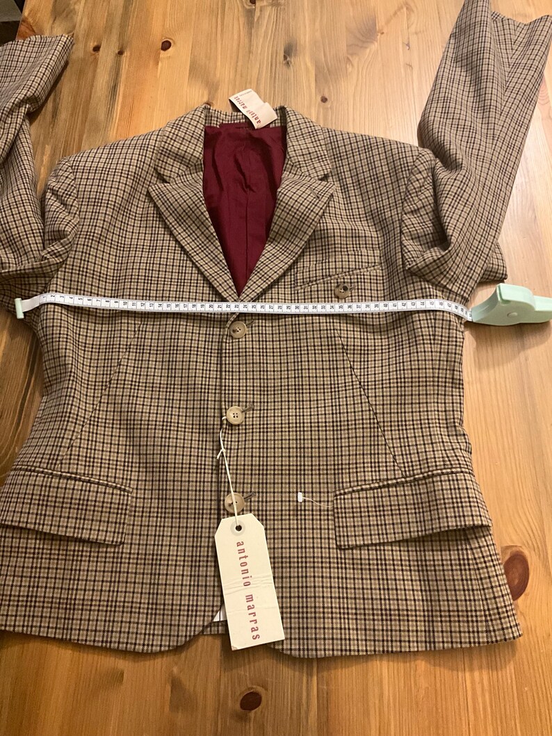 Puede incluir: Una blazer a cuadros marr&oacute;n y beige con forro burdeos. La blazer tiene dos bolsillos delanteros, tres botones y una etiqueta "antonio marras". Una cinta m&eacute;trica est&aacute; colocada sobre la blazer.