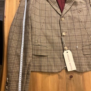Puede incluir: Una blazer a cuadros beige y negro con forro burdeos. La blazer tiene dos botones y una etiqueta que dice "antonio marras". Una cinta m&eacute;trica est&aacute; al lado de la blazer, mostrando una longitud de aproximadamente 173 cm.