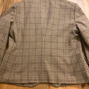 Puede incluir: Un blazer a cuadros marr&oacute;n y negro con solapas y cierre de dos botones. Se ve la parte trasera del blazer, mostrando un corte entallado y una abertura central. La tela tiene un patr&oacute;n tejido cl&aacute;sico.