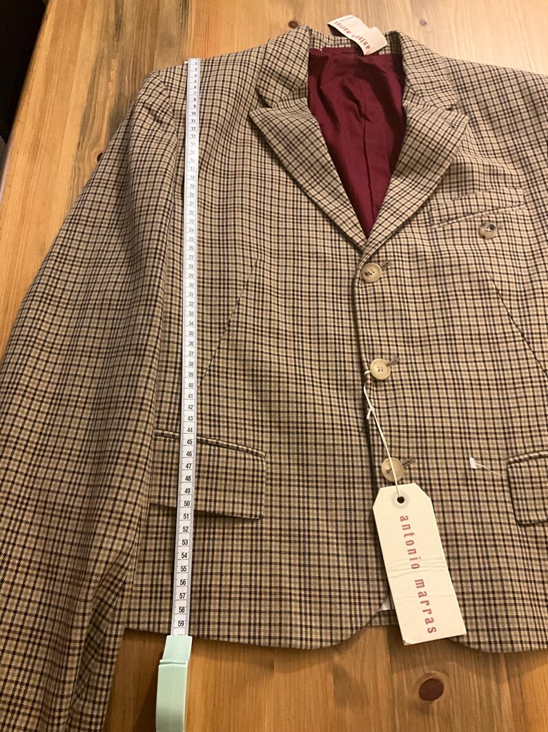 Puede incluir: Una blazer a cuadros marr&oacute;n y beige con forro burdeos. La blazer tiene dos bolsillos delanteros y tres botones. Una cinta m&eacute;trica muestra que la blazer mide aproximadamente 58 cm de largo. La etiqueta dice "antonio marras".