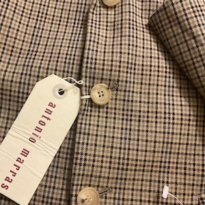 Puede incluir: Primer plano de una blazer a cuadros marr&oacute;n y beige con tres botones color crema. La blazer tiene una etiqueta que dice "antonio marras". La tela tiene un sutil patr&oacute;n de cuadros azules.