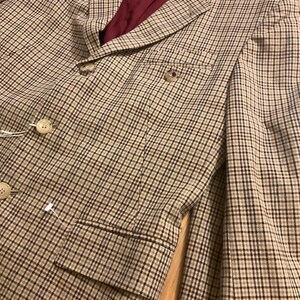 Puede incluir: Un blazer a cuadros marr&oacute;n y beige con forro burdeos. El blazer tiene dos botones y un bolsillo en el pecho. La tela tiene un sutil estampado de cuadros. Un estilo cl&aacute;sico.