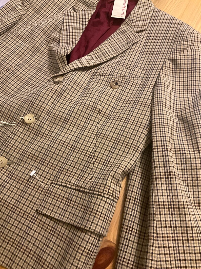 Puede incluir: Un blazer a cuadros marr&oacute;n y beige con forro burdeos. El blazer tiene dos botones y un bolsillo en el pecho. La tela tiene un sutil estampado de cuadros. Un estilo cl&aacute;sico.
