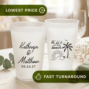 May include: Two frosted plastic cups featuring black printed designs. One cup displays the names Kathryn & Matthew with the date 05.23.27. The other cup features a palm tree, sun, ocean waves, and the text We did it on the beach.
