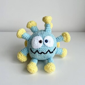 Peut inclure: Un jouet fait à la main en crochet représentant une créature bleue et jaune. Il présente de grands yeux blancs et bleus, une bouche en zigzag noire et de multiples appendices jaunes.