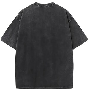 May include: A short-sleeve t-shirt in a washed-out charcoal black colour. The garment features a crew neckline, dropped shoulder seams, and a relaxed fit. The fabric has a mottled, uneven texture throughout, giving it a faded, worn-in appearance.