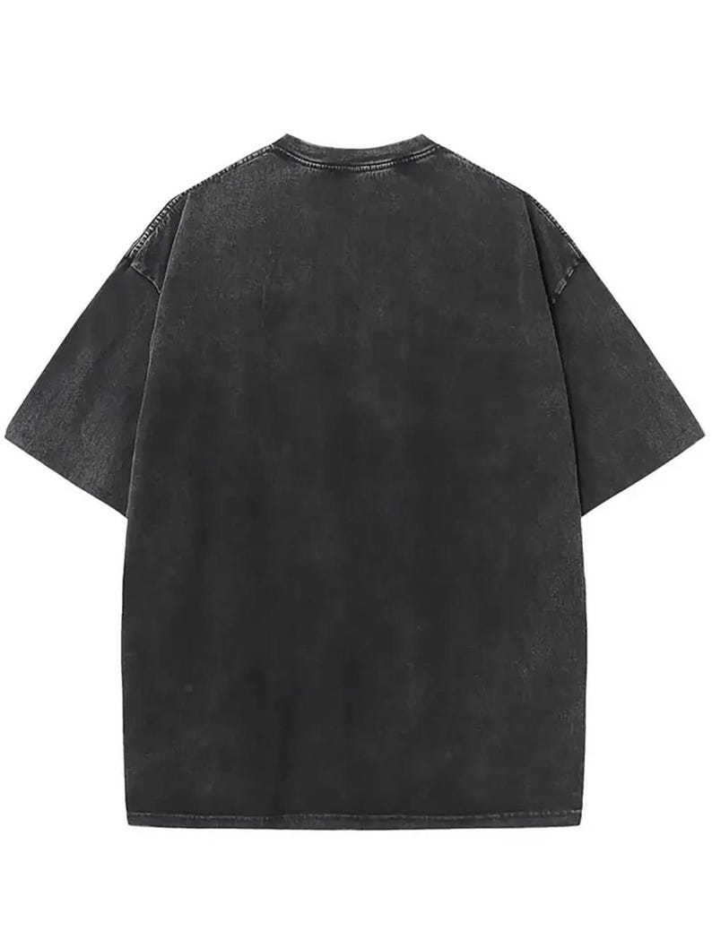 May include: A short-sleeve t-shirt in a washed-out charcoal black colour. The garment features a crew neckline, dropped shoulder seams, and a relaxed fit. The fabric has a mottled, uneven texture throughout, giving it a faded, worn-in appearance.