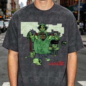 May include: A charcoal grey acid-wash t-shirt featuring a graphic print of the band Gorillaz. The design displays four animated characters in green tones, with the red Gorillaz logo printed in the bottom right corner of the graphic illustration.