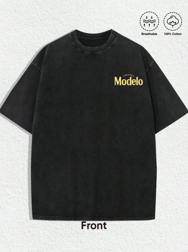 May include: A black short-sleeve t-shirt with a crew neckline and a washed-out finish. The chest features the yellow text "Cerveza Modelo". Two circular icons in the top right corner indicate the shirt is breathable and made of 100% cotton.