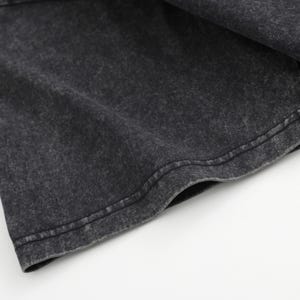 May include: A short-sleeved t-shirt featuring a dark charcoal gray fabric with a washed-out, mottled texture. The garment has a visible stitched hem along the sleeve edge, showcasing a consistent, weathered appearance across the material surface.