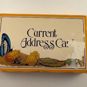 May include: A rectangular box for Current Address Cards with a cream-colored top featuring a blue butterfly perched on yellow flowers. The text Current Address Cards is printed in black. The box has a yellow border and shows signs of wear.