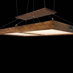 May include: A rectangular pendant light fixture featuring a dark stained wood frame with a visible grain pattern. The light has a flat, white diffuser panel and is suspended by thin metal cables from a matching rectangular wooden ceiling mount.