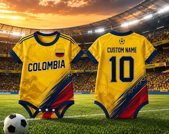 May include: Two yellow baby bodysuits with the word "COLOMBIA" and the number "10" printed on them. The bodysuits have blue and red accents, and a small Colombian flag. A soccer ball rests on the green grass in front of the bodysuits.