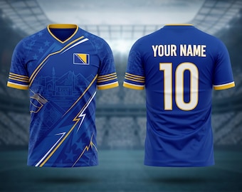 May include: A blue soccer jersey with yellow and white accents. The front features a design with a flag, stars, and architectural elements. The back displays "YOUR NAME" above the number "10".
