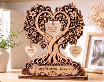 May include: A wooden decorative sculpture featuring two intertwined tree trunks forming a heart shape with intricate floral carvings. Three heart-shaped wooden tags hang from the branches, engraved with names and dates. The base reads Happy Wedding Anniversary.