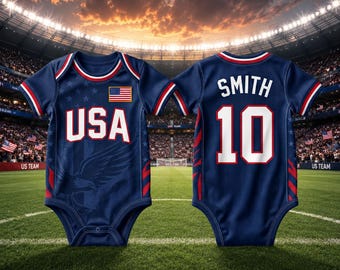 May include: Two navy blue baby bodysuits, one front and one back view, with red and white accents. The front bodysuit has "USA" in white block letters and an American flag patch. The back has "SMITH 10" in white.