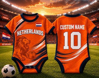 May include: Orange baby bodysuit with navy blue trim, featuring "NETHERLANDS" text, a lion graphic, and a soccer ball. The back displays "CUSTOM NAME" and the number 10. A soccer ball rests on the grass.