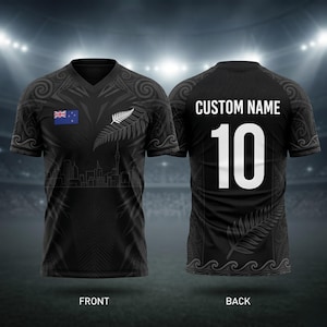 Könnte beinhalten: Schwarzes Rugby-Trikot mit der neuseeländischen Flagge, einem Silberfarn und einem Skyline-Motiv. Auf der Rückseite sind die Nummer 10 und Platz für einen individuellen Namen zu sehen. Vorder- und Rückseite sind abgebildet.