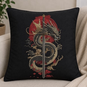 Könnte beinhalten: Ein quadratisches schwarzes Zierkissen mit einer Stickerei eines langen, gewundenen Drachen in Gold- und Schwarztönen, der sich um ein vertikales silbernes Schwert windet. Hinter dem Drachen befindet sich ein großer, roter Kreis auf schwarzem Grund.