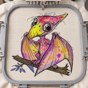 Könnte beinhalten: Ein Stickdesign in einem grauen Kunststoffrahmen zeigt einen farbenfrohen Flugsaurier mit großen Augen, gelbem Schnabel sowie pinken, orangen und violetten Flügeln, der auf einem braunen Ast mit kleinen blauen Blättern auf hellem Stoff sitzt.