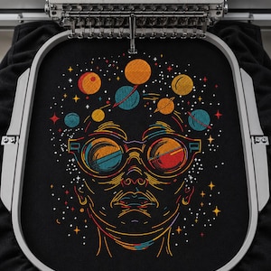 Könnte beinhalten: Ein Stickrahmen mit schwarzem Stoff und einem farbenfrohen Stickmotiv eines Gesichts mit runder Brille. Über dem Kopf befinden sich verschiedene Planeten und Sterne aus orangefarbenem, blauem und gelbem Garn. Die Stickmaschinennadel ist oben sichtbar.