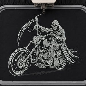 May include: A black fabric panel secured in a rectangular embroidery hoop featuring a detailed white thread embroidery of a skeleton wearing a hooded cloak, riding a motorcycle and holding a large scythe above its head while driving forward.