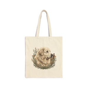 May include: Cream-colored tote bag featuring a golden retriever illustration. The dog's portrait is surrounded by a wreath of green and yellow foliage. The bag has a rectangular shape with two long handles.
