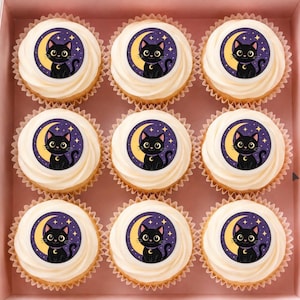 May include: A set of nine cupcakes arranged in a square grid within a pink box. Each cupcake features a white frosting swirl topped with a circular edible topper displaying a black cat sitting in front of a yellow crescent moon and stars.