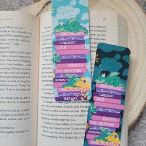 May include: Two dragon-themed bookmarks. One shows a dragon on a stack of books with titles such as "Dragonology" and "Treasure." The other has a similar design but with a dark background.