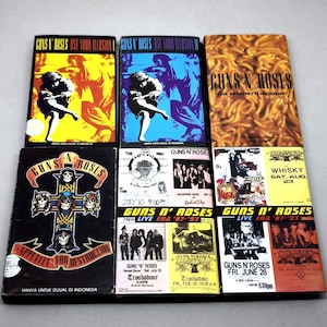 May include: A selection of Guns N' Roses album covers and concert flyers. The album covers include "Use Your Illusion" in yellow and blue, "The Spaghetti Incident?", and "Appetite for Destruction". Concert flyers feature dates and venues.