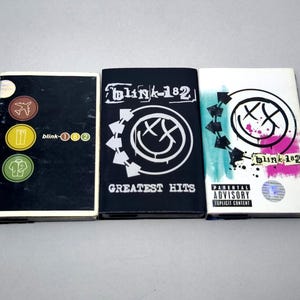 May include: Three Blink-182 CD cases. The first is black with icons and text. The second is black with the band's logo and "GREATEST HITS". The third is white with the band's logo, text, and a parental advisory warning.